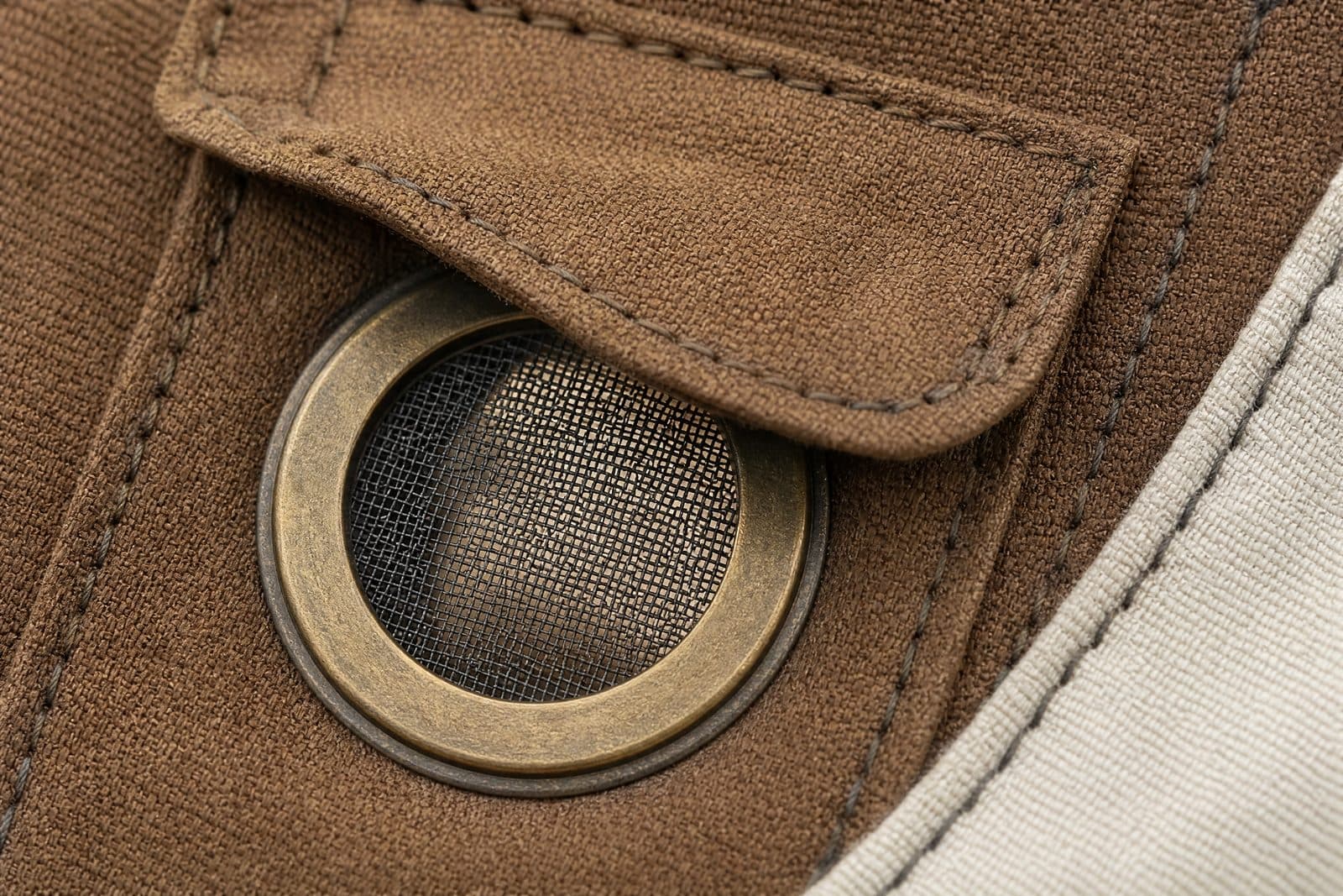 A circular mesh vent set into marine canvas, with a brass rim, a fine mesh screen and a storm flap stitched above it.
